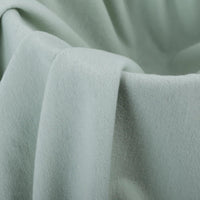 Un gros plan de la Flanelle de coton uni au mètre de Longon Craft France montre sa couleur vert clair, sa texture super douce et ses plis délicats - une flanellette ultra-confortable parfaite pour pyjamas et câlins d'automne.