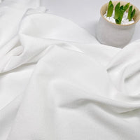 Gros plan sur le Tissu seersucker uni texturé au mètre de Longan Craft France, drapé sur une surface, avec une petite plante en pot avec des feuilles vertes et des cailloux blancs dans le coin supérieur droit.