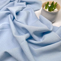Le Tissu seersucker uni texturé au mètre de Longan Craft France, présenté à côté d'une petite plante grasse dans un pot en céramique blanc sur une surface blanche, est idéal pour créer des vêtements d'été.