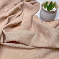 Le Tissu seersucker uni texturé au mètre de Longan Craft France, en polyester froissé à carreaux beige, est présenté avec de douces ondulations près d'une plante en pot blanc sur une surface claire, idéal pour des vêtements d'été.