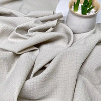 Gros plan sur le tissu polyester seersucker beige clair de Longan Craft France, drapé librement à côté d'un pot en céramique blanc moucheté contenant une petite plante succulente verte sertie de pierres blanches.