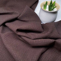 Un morceau de Longan Craft France Tissu seersucker uni texturé au mètre est présenté à côté d'un petit pot en céramique blanche avec une succulente verte et des galets blancs.