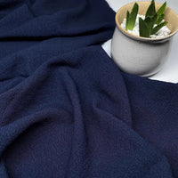 Un tissu en seersucker bleu de Longan Craft France est présenté à côté d'un pot en céramique blanc moucheté avec une succulente verte et des galets blancs.