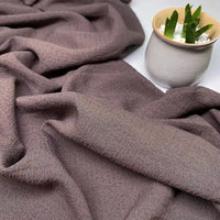 Gros plan sur le Tissu seersucker uni texturé au mètre de Longan Craft France, drapé sur une surface, avec un petit pot blanc contenant une succulente verte dans le coin supérieur droit.