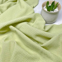 Le tissu Longan Craft France Tissu seersucker uni texturé au mètre, un tissu de polyester à carreaux vert clair, est présenté à plat à côté d'une petite plante succulente en pot dans un pot de céramique blanc avec des galets blancs.