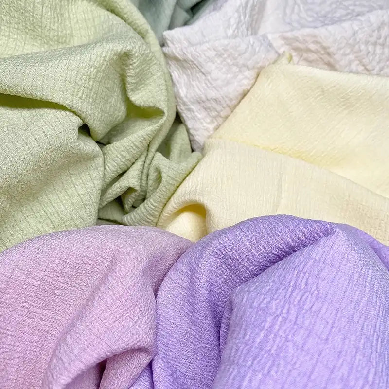 Le tissu seersucker souple vert, blanc, jaune et violet de Longan Craft France présente des surfaces texturées et froissées, idéales pour les vêtements d'été. Disponible au mètre en polyester uni ou à carreaux.