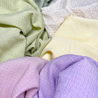 Le tissu seersucker souple vert, blanc, jaune et violet de Longan Craft France présente des surfaces texturées et froissées, idéales pour les vêtements d'été. Disponible au mètre en polyester uni ou à carreaux.