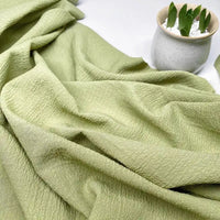 Le tissu seersucker uni texturé au mètre de Longan Craft France, en polyester à carreaux froissés, est étalé sur une surface. Un petit pot blanc avec un succulent vert ajoute une touche estivale idéale pour vêtements d'été.