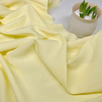 Un tissu texturé en polyester à carreaux seersucker jaune clair de Longan Craft France est présenté à côté d'un pot beige avec une succulente verte et des galets blancs.