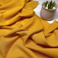 Un tissu seersucker jaune moutarde de Longan Craft France est posé à côté d'un pot en céramique blanc contenant une succulente verte - parfait pour confectionner des vêtements d'été. Achetez le Tissu seersucker uni texturé, froissé, ou à carreaux au mètre.