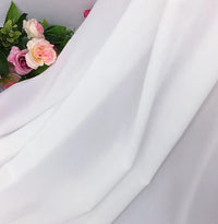 Des roses artificielles roses et blanches avec des feuilles vertes sont partiellement recouvertes par la mousseline extensible au mètre (mousseline polyester épaisse et extensible) de Longan Craft France, drapée doucement dans le coin supérieur gauche de l'image.
