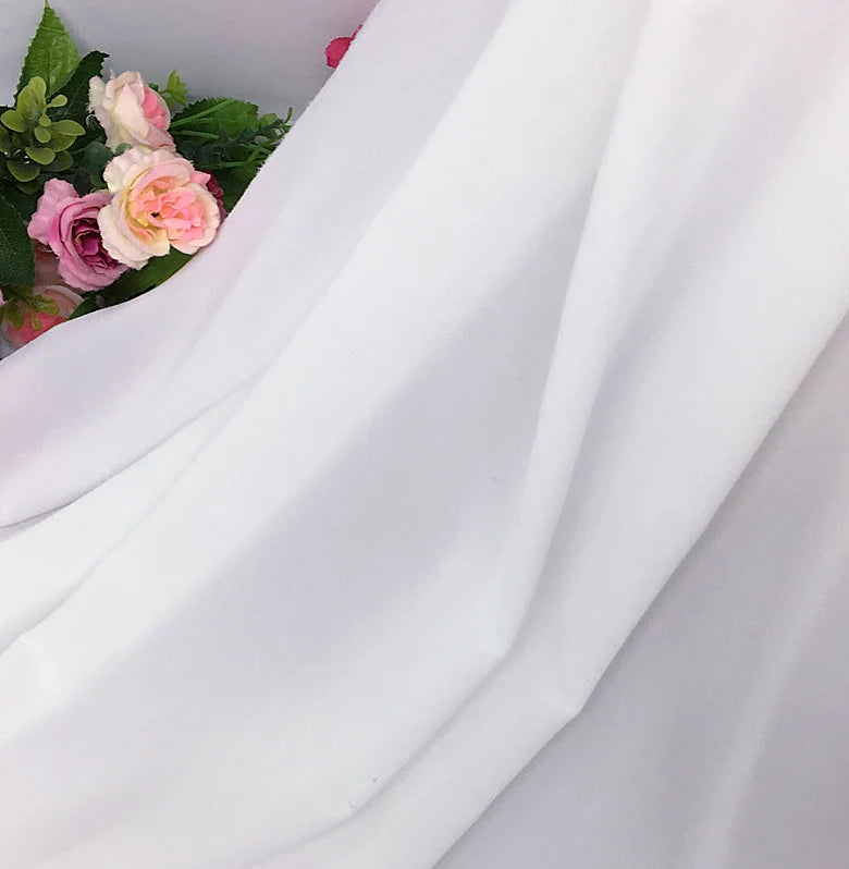 Des roses artificielles roses et blanches avec des feuilles vertes sont partiellement recouvertes par la mousseline extensible au mètre (mousseline polyester épaisse et extensible) de Longan Craft France, drapée doucement dans le coin supérieur gauche de l'image.