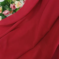 Une Mousseline rouge vif extensible au mètre de Longan Craft France est drapée en diagonale, avec des fleurs artificielles roses et jaunes et des feuilles vertes dans le coin supérieur gauche.