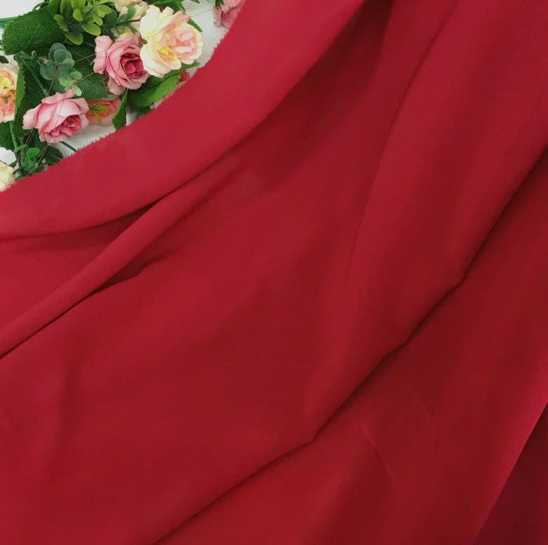 Une Mousseline rouge vif extensible au mètre de Longan Craft France est drapée en diagonale, avec des fleurs artificielles roses et jaunes et des feuilles vertes dans le coin supérieur gauche.