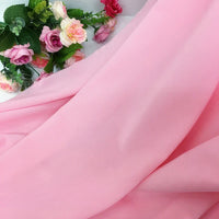 Une longueur de Mousseline extensible au mètre de Longan Craft France en rose clair est délicatement drapée à côté de fleurs artificielles dans les tons rose et vert.