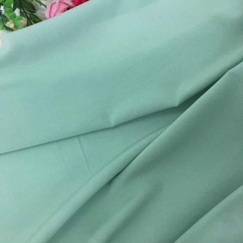 Gros plan sur la Mousseline extensible au mètre de Longan Craft France, une mousseline de polyester vert clair à la texture lisse et extensible. Ses plis souples et ses accents floraux la rendent idéale pour la confection de robes élégantes ou les projets créatifs.