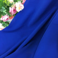 Des fleurs artificielles roses, jaunes et blanches avec des feuilles vertes sont disposées sur la Mousseline extensible au mètre de Longan Craft France, une mousseline épaisse en polyester extensible - idéal tissu pour robe.