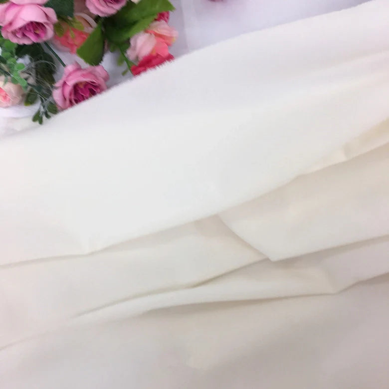 Gros plan sur la Mousseline extensible au mètre (épaisse et extensible) de Longan Craft France en blanc, avec des fleurs artificielles roses et violettes disposées dans le coin supérieur gauche.