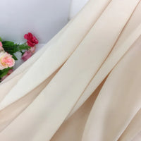 Gros plan sur la Mousseline extensible au mètre de couleur crème de Longan Craft France, un épais tissu de polyester extensible drapé en plis souples avec des fleurs artificielles roses et rouges sur le côté.