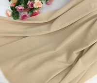 Un morceau de Mousseline beige extensible au mètre de Longan Craft France est délicatement plié, avec des roses artificielles roses et rouges et des feuilles vertes présentées dans le coin supérieur gauche du tissu polyester épais et extensible.