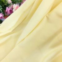 Gros plan sur la Mousseline extensible au mètre de Longan Craft France, en polyester jaune clair aux plis délicats, entourée de fleurs artificielles roses et blanches et de feuillage vert - idéale pour confectionner des robes élégantes.