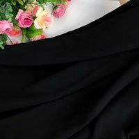 Un tissu noir épais et extensible en polyester Mousseline de Longan Craft France est drapé sur la majeure partie de l'image, tandis qu'un bouquet de fleurs roses, pêches et blanches avec des feuilles vertes apparaît dans le coin supérieur gauche.
