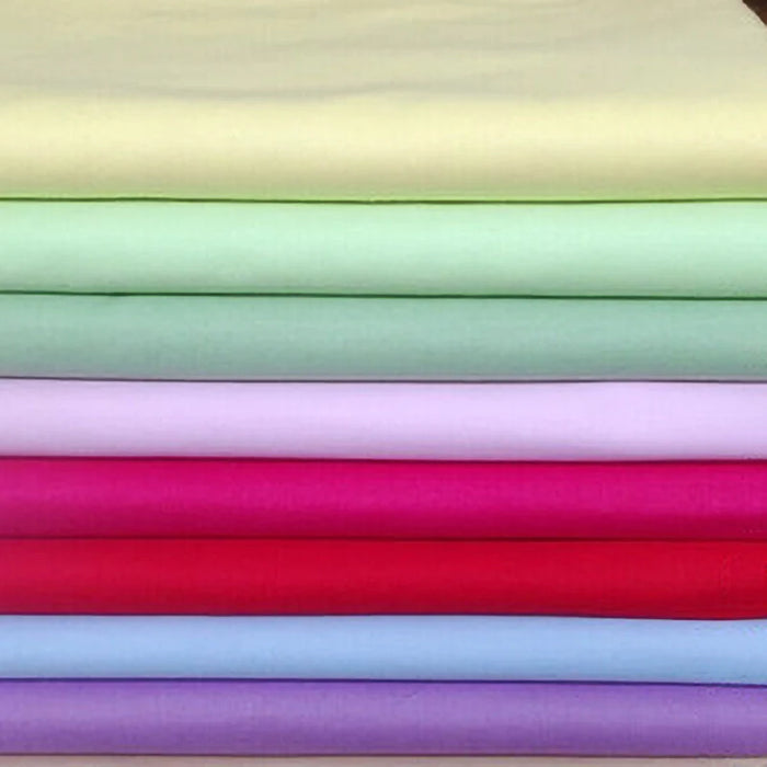Une pile de Longan Craft France Popeline de coton extensible au mètre en jaune clair, vert, violet, rose, rouge et bleu - idéal pour les chemises, les robes, les doublures, les projets de couture et les loisirs créatifs.