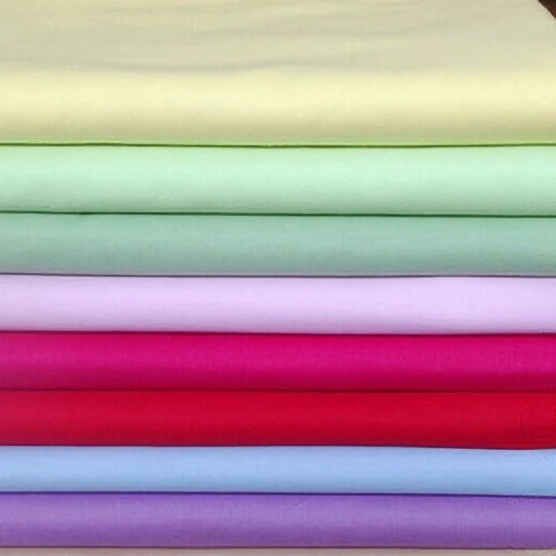 Une pile de Longan Craft France Popeline de coton extensible au mètre en jaune clair, vert, violet, rose, rouge et bleu - idéal pour les chemises, les robes, les doublures, les projets de couture et les loisirs créatifs.