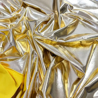 Tissu lamé brillant et froissé, argenté et doré, stretch au mètre, de Longan Craft France, avec des touches de jaune dans les coins. Le polyester réfléchissant évoque les costumes luxueux et les projets créatifs.