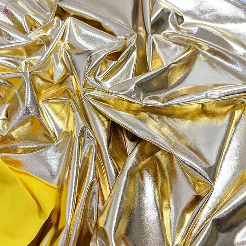 Tissu lamé brillant et froissé, argenté et doré, stretch au mètre, de Longan Craft France, avec des touches de jaune dans les coins. Le polyester réfléchissant évoque les costumes luxueux et les projets créatifs.