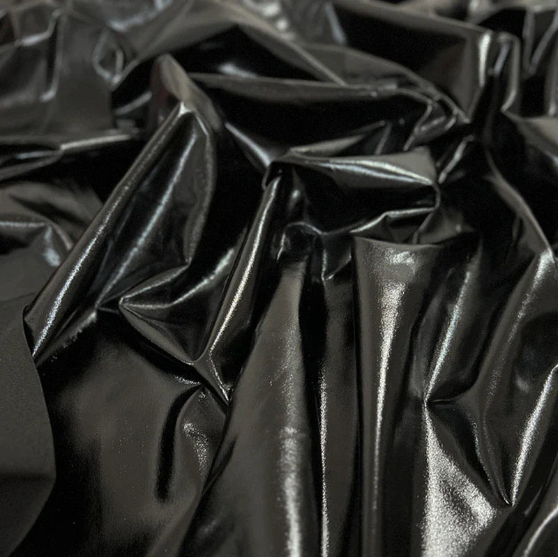 Gros plan sur le tissu lamé noir brillant stretch au mètre de Longan Craft France, montrant sa surface en polyester réfléchissant avec des plis irréguliers - idéal pour la couture, les loisirs créatifs, la tapisserie et les costumes de scène.