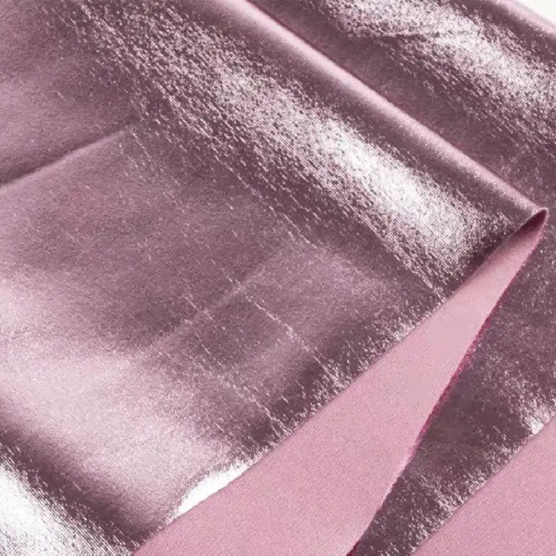 Gros plan sur le Tissu lamé stretch au mètre de Longan Craft France : tissu de polyester rose métallisé et brillant avec une finition lisse et lustrée, idéal pour la couture, les projets de bricolage et l'ameublement. On voit les plis qui mettent en valeur sa surface réfléchissante.