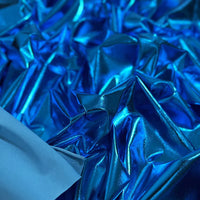 Gros plan sur un tissu lamé stretch au mètre de Longan Craft France, composé d'un tissu polyester réfléchissant dans différentes nuances de bleu et d'une petite section de tissu bleu mat. Idéal pour la couture, l'artisanat et l'ameublement.