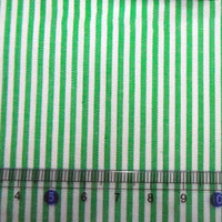 Gros plan sur le tissu en popeline de coton rayé au mètre de Longan Craft France - 100 % coton, popeline 40S teinte en fil avec des rayures vertes. Une règle transparente avec des marques bleues et les chiffres 4 à 10 est placée en bas pour l'échelle.