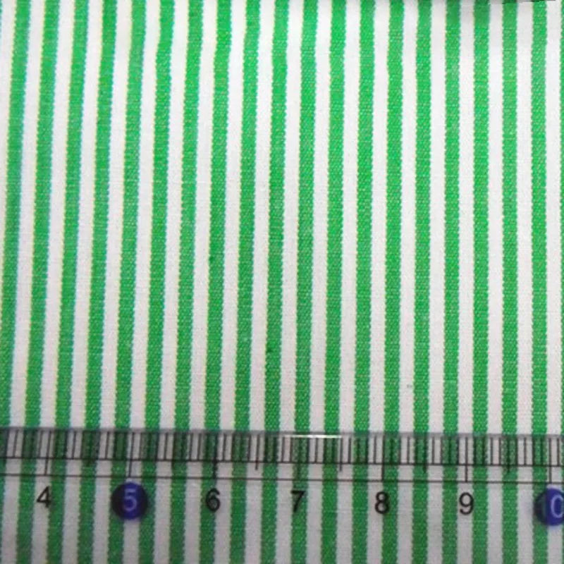Gros plan sur le tissu en popeline de coton rayé au mètre de Longan Craft France - 100 % coton, popeline 40S teinte en fil avec des rayures vertes. Une règle transparente avec des marques bleues et les chiffres 4 à 10 est placée en bas pour l'échelle.