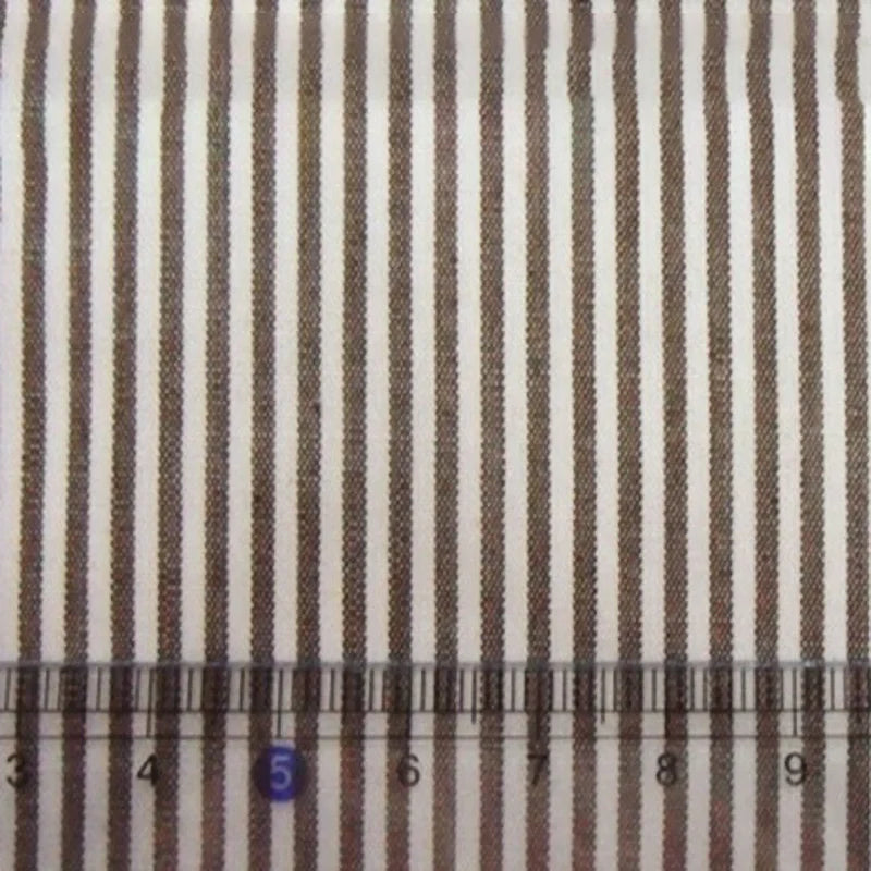 Gros plan sur des rayures teintes au fil sur un tissu en popeline de coton rayé au mètre de Longan Craft France (Tissu en popeline de coton rayé au mètre) ; alternance de rayures brunes et blanches avec une règle transparente indiquant 1 à 10 cm en bas.