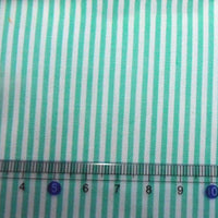 Une règle de 4 à 10 cm est placée sur un tissu en popeline de coton rayé au mètre, turquoise et blanc (Longan Craft France), idéal pour les chemises, les robes et les nappes.