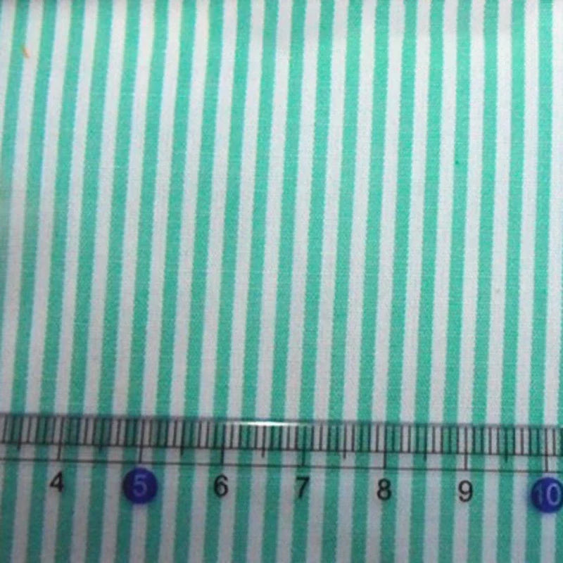 Une règle de 4 à 10 cm est placée sur un tissu en popeline de coton rayé au mètre, turquoise et blanc (Longan Craft France), idéal pour les chemises, les robes et les nappes.