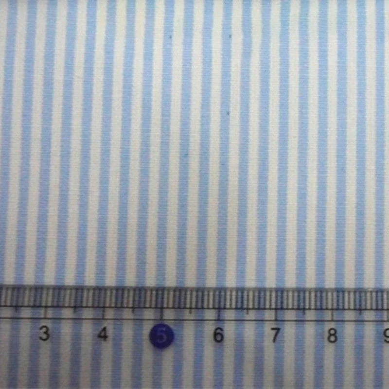 Un gros plan du Tissu en popeline de coton rayé au mètre de Longan Craft France montre des rayures bleues et blanches teintes en fil, avec une règle transparente en dessous affichant des mesures de 3 à 8 cm.