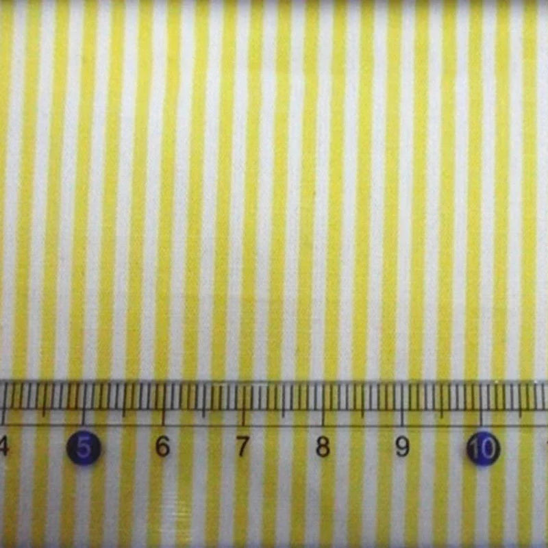 Gros plan sur les rayures jaunes et blanches du Tissu en popeline de coton rayé au mètre de Longan Craft France, avec une règle en dessous indiquant 5 à 10 cm, idéal pour les chemises, les robes et les nappes.