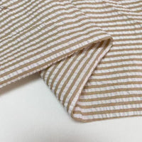 Un gros plan du Seersucker rayé au mètre de Longan Craft France montre son tissu rayé beige et blanc en polyester-coton, plié avec des lignes horizontales - un tissu seersucker idéal pour l'été, parfait pour les vêtements d'été légers et aérés.