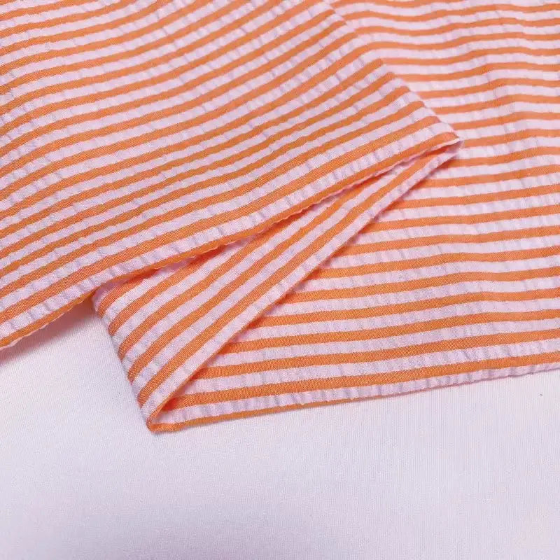 Un gros plan du Seersucker rayé au mètre de Longan Craft France montre des rayures horizontales colorées et un bord plié - idéal comme tissu seersucker polyester-coton léger pour une tenue d'été confortable et aérée.