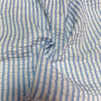 Gros plan sur le Seersucker rayé au mètre de Longan Craft France : tissu rayé bleu clair et blanc en polyester-coton, texture douce avec des plis, idéal pour l'été, avec des rayures colorées régulièrement espacées.