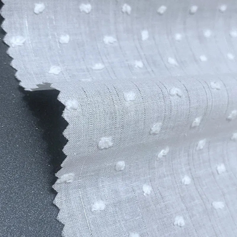 Gros plan sur le Voile plumetis au mètre de Longan Craft France - un voile de coton blanc suisse à pois avec des points texturés et des bords coupés en zigzag, légèrement transparent, idéal pour la couture, les projets créatifs et la décoration d'intérieur.
