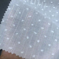 Un gros plan du Voile plumetis au mètre de Longan Craft France montre son tissu de coton blanc à pois avec des rayures brillantes et un bord festonné - idéal pour la décoration intérieure, la couture et les loisirs créatifs.