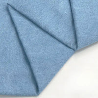 Gros plan sur le tissu en jean coton lavé 14,5 oz au mètre de Longan Craft France en bleu clair, soigneusement plié pour montrer la texture et le tissage de ce denim épais, parfait pour les jeans.