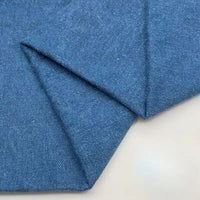 Un gros plan du Tissu en jean coton lavé 14,5 oz au mètre de Longan Craft France montre un denim bleu épais, soigneusement plié avec une trame diagonale visible, idéal pour la fabrication de jeans.
