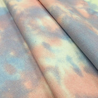 Gros plan sur le Tissu denim en coton tie-dye au mètre de Longan Craft France, un denim de 10 oz en pêche pastel, lavande et bleu pâle, dont la texture fine et les teintes délicatement mélangées sont parfaites pour des vêtements en jean vibrants faits à la main.