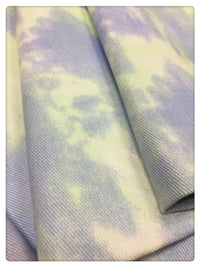 Gros plan sur le denim tie-dye en coton de 10 oz de Longan Craft France, vendu au mètre. Ce tissu coloré est tissé en sergé et présente un motif violet et jaune pastel. Il est idéal pour la décoration ou la confection de vêtements en denim uniques.