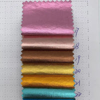 Une carte d'échantillons de Longan Craft France présente six échantillons verticaux de "Tissu lamé métallisé froissé au mètre" en rose, bronze, cuivre, or, jaune et turquoise sur papier blanc avec des numéros écrits à la main. Idéal pour la couture et l'artisanat créatif.